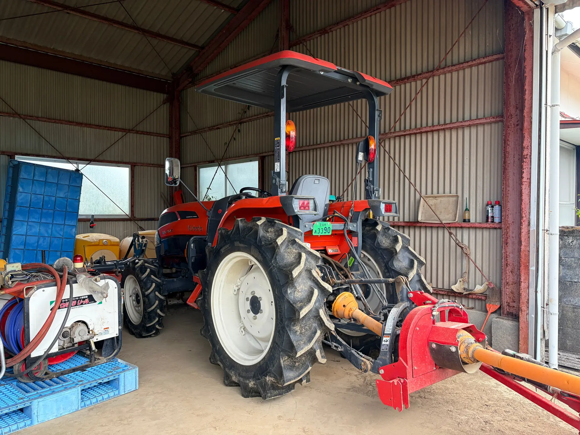 熊本県玉名市にある株式会社Ueda Farmが使用するトラクター。草刈り用アタッチメントを装着し、納屋に停められた車体全体の様子